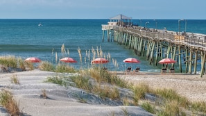 Une plage avec une jetée en bois, des parasols rouges et un kiosque.