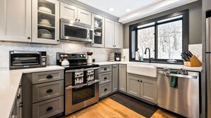 Een moderne keuken met roestvrijstalen apparatuur, witte kasten en een groot raam dat zorgt voor veel daglicht.