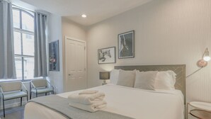 A hotel room with a large bed, a bedside table, a lamp, and a window with curtains. - Luxurious 1BR in FIDI Boston | Close to Everything (Boston)