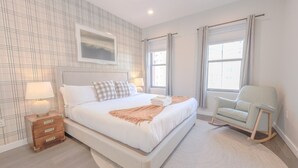 Une chambre à coucher moderne avec un grand lit, une table de chevet, un fauteuil à bascule et une fenêtre avec des rideaux.