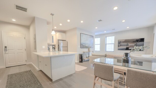 Une cuisine moderne avec des meubles blancs, un îlot central et un coin repas comprenant une table et des chaises en verre.