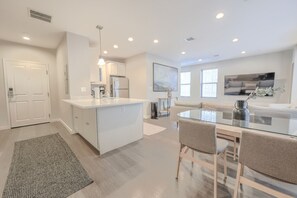 A modern kitchen with white cabinetry, a central island, and a dining area with a glass table and chairs. - Luxury Loft | W/D in Unit | Pet Friendly (Boston)
