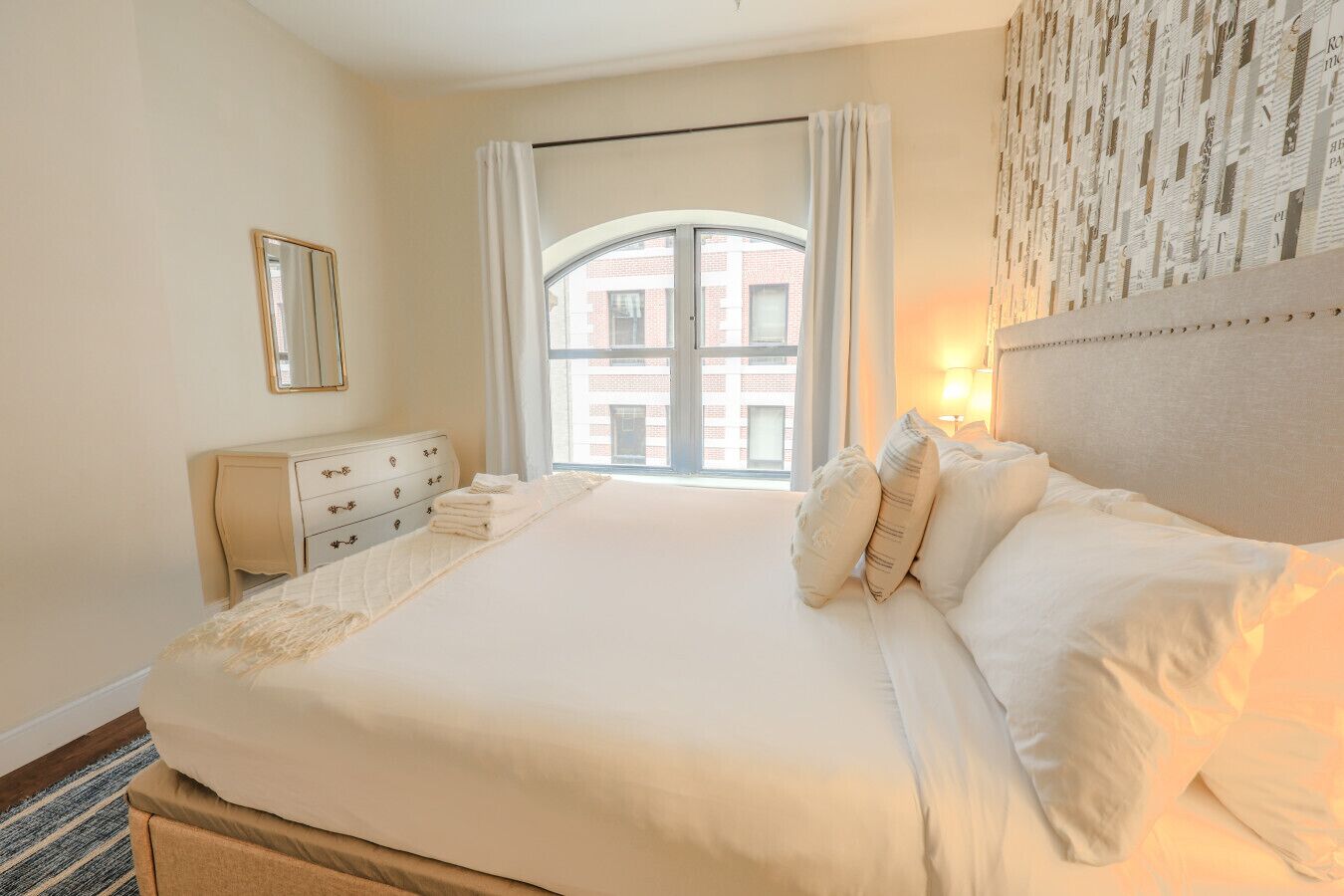 Une chambre d’hôtel avec un grand lit, une commode, un miroir et une fenêtre avec des rideaux.