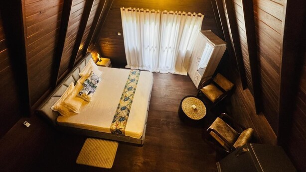 Une chambre confortable située dans les combles, avec un lit, des oreillers, une petite table sur laquelle est posée une bougie, et une chaise.