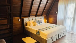 Une chambre avec un plafond en pente en bois, un lit recouvert d’une couvre-lit à motifs et une table de chevet.