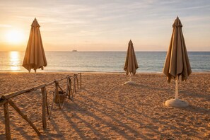 Een strand met twee parasols en een houten omheining.