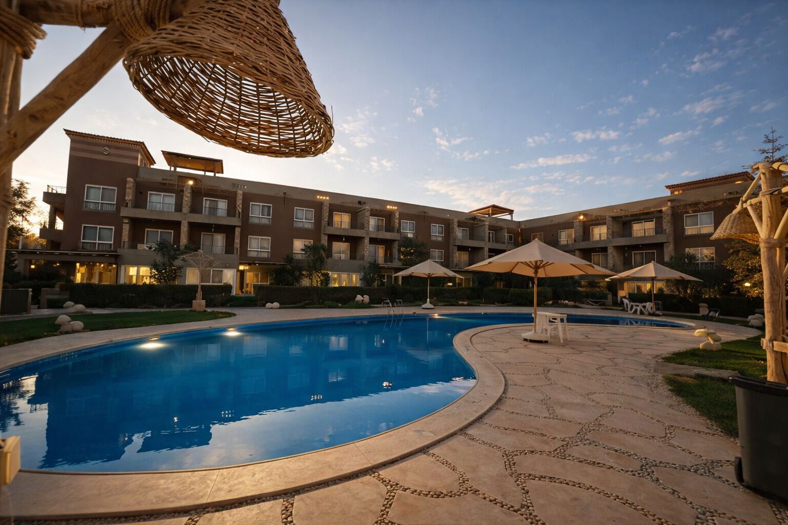 A swimming pool with lounge chairs and umbrellas, surrounded by a courtyard with a multi-story building.