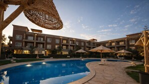 Una piscina con sillones de baño y sombrillas, rodeada por un patio con un edificio de varios pisos.