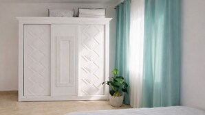 Un dormitorio con cama, armario, planta y ventana con cortinas.