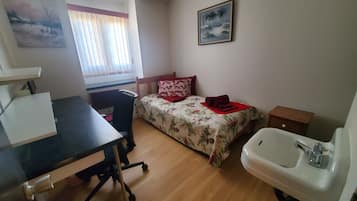 Una habitación pequeña y ordenada con una cama, un escritorio y un lavabo.