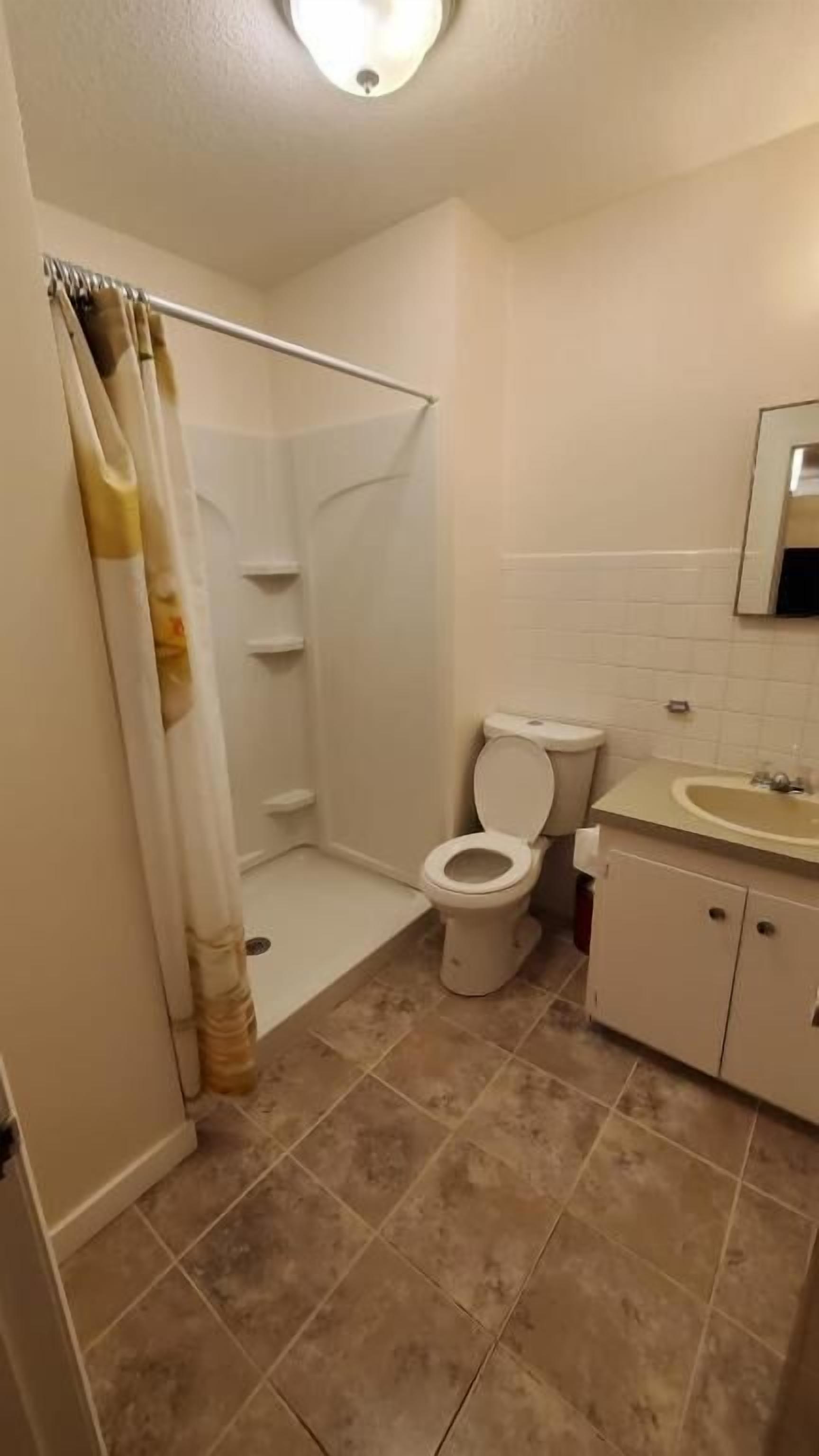 Badeværelse med brusebad, toilet, håndvask og skab.