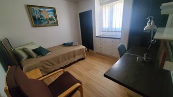 Una habitación pequeña y poco amueblada con una cama, un escritorio, una silla, una ventana con persianas y un cuadro en la pared.