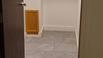 Una habitación con puerta, una lámpara en el techo, una puerta de madera, un armario pequeño de madera y piso de baldosas.