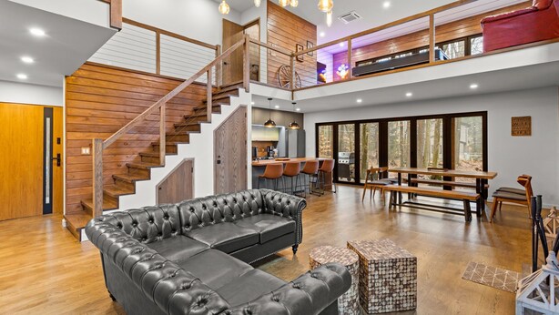 A spacious living area with a black leather sofa, wooden staircase, and a dining area with a bench and chairs. - Superb 6-bedroom house with HVAC in charming Pocono Pines (Pocono Pines)