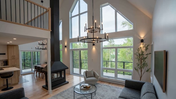 A spacious living area with a fireplace, large windows, and a high ceiling. - New Construction | Spa & Pool Table | Le Foresti (Saint-Alphonse-Rodriguez)