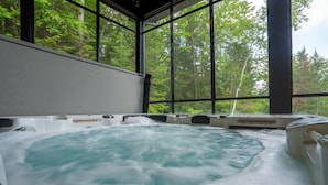 A hot tub with a view of a forest through large windows. - New Construction | Spa & Pool Table | Le Foresti (Saint-Alphonse-Rodriguez)