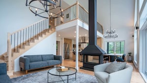 A spacious living area with a staircase, a fireplace, and a dining area. - New Construction | Spa & Pool Table | Le Foresti (Saint-Alphonse-Rodriguez)