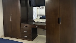 A bedroom with a large wardrobe, a desk with a flat-screen TV, and a bed with a blue cover. - SPACIOUS CONDOMINIUM, CLOSE TO AIRPORT (Hermosillo)