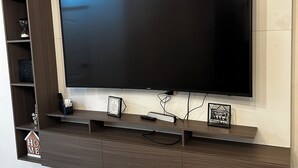 A modern living room with a large flat-screen TV mounted on a wooden wall unit. - SPACIOUS CONDOMINIUM, CLOSE TO AIRPORT (Hermosillo)