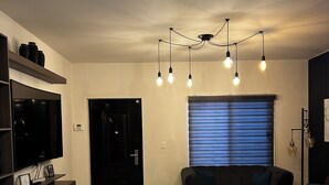A modern living room with a flat-screen TV, a sofa, a coffee table, and a unique ceiling light fixture. - SPACIOUS CONDOMINIUM, CLOSE TO AIRPORT (Hermosillo)