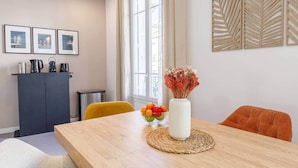 Un comedor con una mesa de madera, un florero con flores y un frutero.