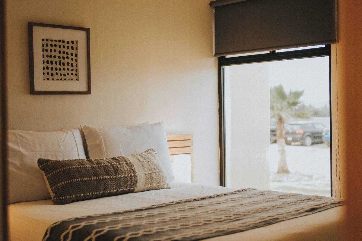 A bedroom with a bed, pillows, a blanket, a framed picture on the wall, and a window with a view of the outside.