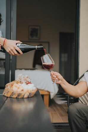 A person pouring wine into a glass held by another person. There is a wooden table with a basket of bread and cheese in the foreground. - Casas VV (Valle de Guadalupe)