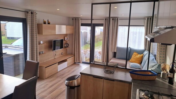 Una cocina moderna con estufa integrada, un comedor con mesa y sillas, y una sala de estar con sofá y cojines.