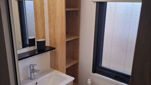 Un baño pequeño con un lavabo blanco, armarios de madera, un espejo y una ventana con persianas.