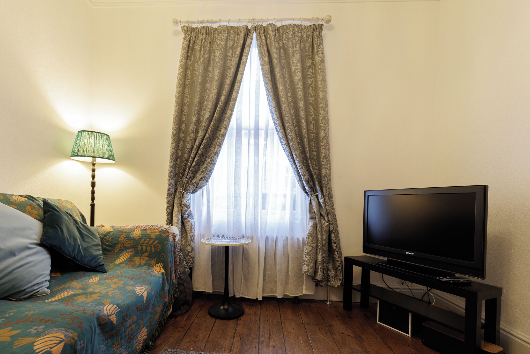 A room with a sofa, a television on a stand, a lamp, and a window with curtains.