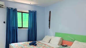 Ein Hotelzimmer mit zwei Betten, einem Fenster mit blauen Vorhängen, einem Deckenventilator und einer grünen Wand.