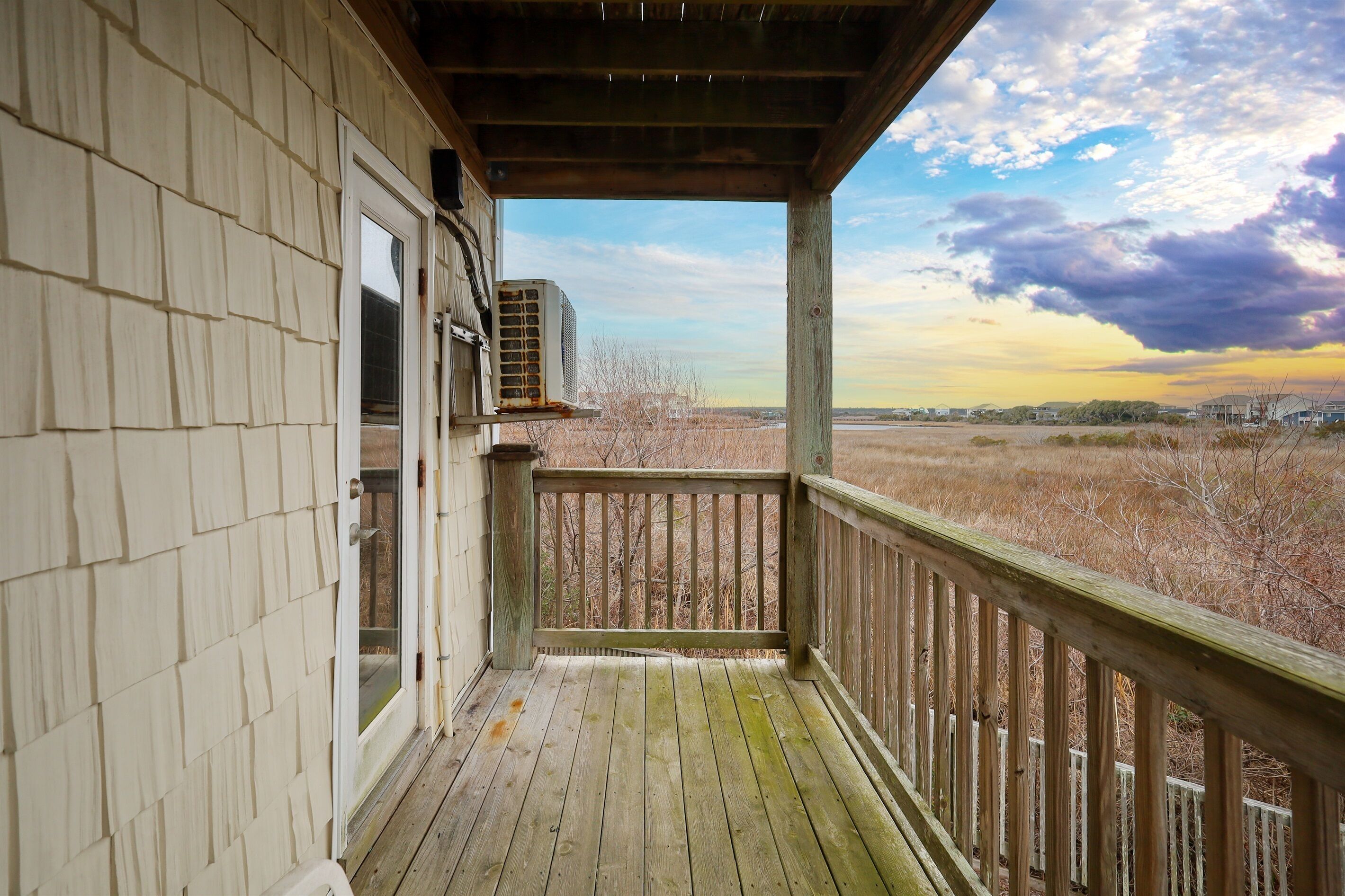 A wooden deck with a view of a field and a cloudy sky.