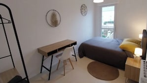Um quarto com uma cama, uma escrivaninha, uma cadeira, uma janela e um radiador.