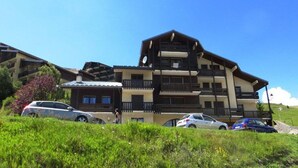 A multi-story hotel with balconies and a sloped roof, surrounded by greenery and parked cars. - 100m from ski slopes, 2nd floor, balcony, tv, ski locker, 45m², Auris en Oisans (Auris)