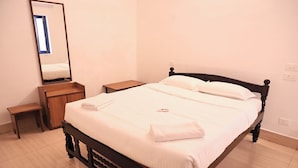 A neatly made bed with white linens, a bedside table, a nightstand, and a mirror on the wall. - Hotel Continental (Puducherry)
