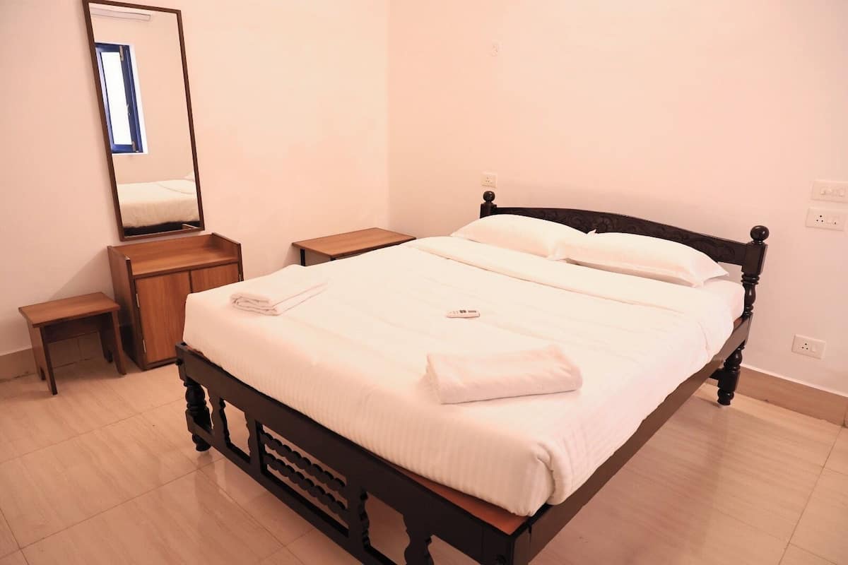A neatly made bed with white linens, a bedside table, a nightstand, and a mirror on the wall.