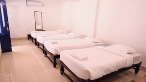 A hotel room with four single beds arranged in a row, a large mirror on the wall, and a blue door. - Hotel Continental (Puducherry)