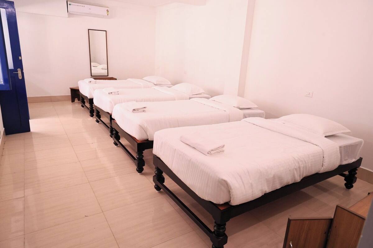 A hotel room with four single beds arranged in a row, a large mirror on the wall, and a blue door.