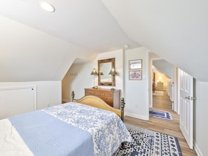 Ein Schlafzimmer mit Bett, Schminktisch, Spiegel und einem zur Treppe führenden Gang.