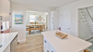 A modern kitchen with white cabinets, a wooden dining table, and a staircase with a glass railing. - Great for Families! Short Drive to Beaches! (Cape May)