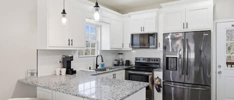 A modern kitchen with white cabinets, a stainless steel refrigerator, a built-in oven, and a granite countertop.