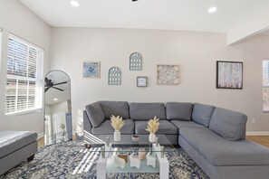 Una sala de estar moderna con un sofá seccional gris, una mesa de centro de vidrio y decoración de pared.