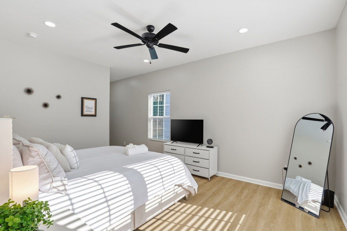 A bedroom with a bed, a dresser, a television, a ceiling fan, and a mirror.