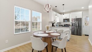 Una cocina moderna con armarios blancos, electrodomésticos de acero inoxidable y un comedor con una mesa y sillas redondas.