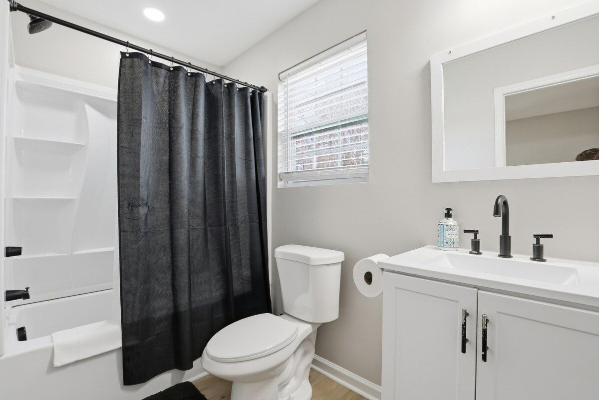 A bathroom with a bathtub, toilet, sink, and a window with blinds.