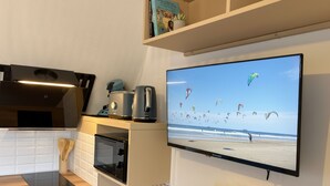 Cuina moderna amb forn integrat, microones i torradora. Un televisor de pantalla plana muntat a la paret mostra una escena de platja amb kites.