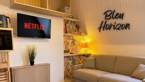 Un saló modern amb un sofà gris, un televisor penjat a la paret que mostra 'NETFLIX' i un rètol 'Blen Horizon'.