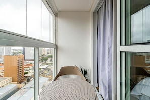 A corner room with a large window, a round table, and a potted plant. - Studio com Vista Para o Centro da Cidade - Man1702 (Curitiba)