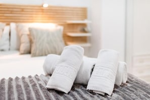 Ein ordentlich gemachtes Bett mit gefalteten Handtüchern, einem hölzernen Kopfstück und einem Nachttisch mit Lampe.