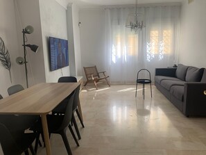 Ein modernes Wohnzimmer mit einem Holzesstisch, schwarzen Stühlen, einem grauen Sofa und einer schwarzen Stehlampe.